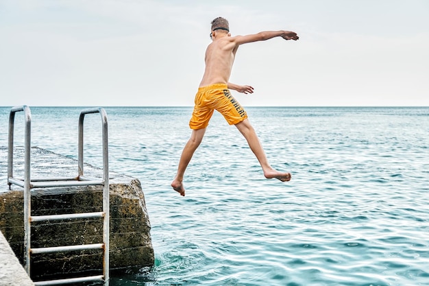Momenten van een jongen die vanaf een stenen pier met een ladder in zee springt en kunstjes doet in gecombineerde beeldreeks