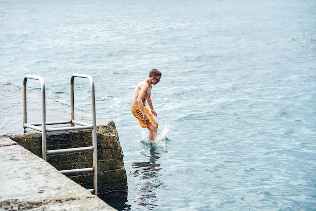Momenten van een jongen die vanaf een stenen pier met een ladder in zee springt en kunstjes doet in gecombineerde beeldreeks