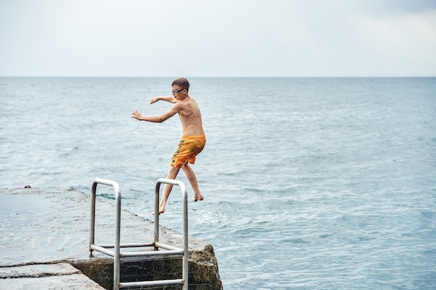 Moments of boy jumping from stone pier with ladder into sea doing tricks in combined image sequence