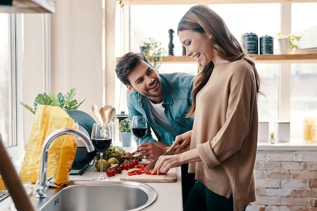 喜びの瞬間。自宅のキッチンに立って夕食を調理する美しい若いカップル