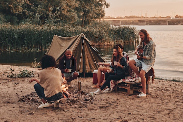 Moments of joy. Group of young people in casual wear smiling while enjoying beach party near the campfire