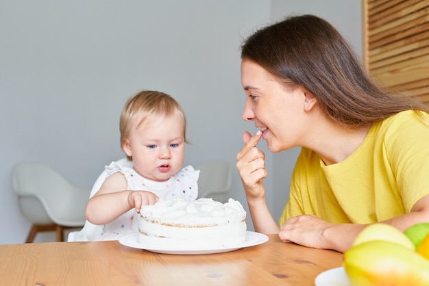 Mommy tasting creamy cake smiling and looking and curious baby sitting on highchair