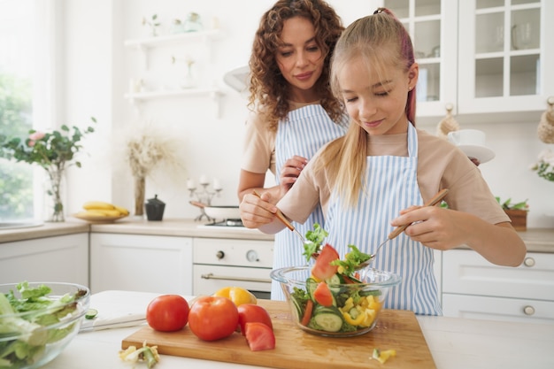 Мама учит свою дочь-подростка готовить овощной салат на кухне