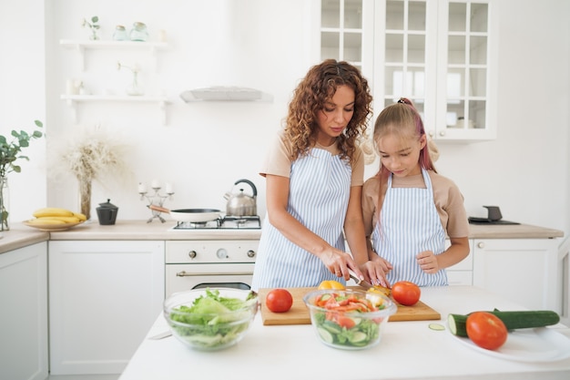 Mommy teaching her teen daughter to cook vegetable salad in kitchen