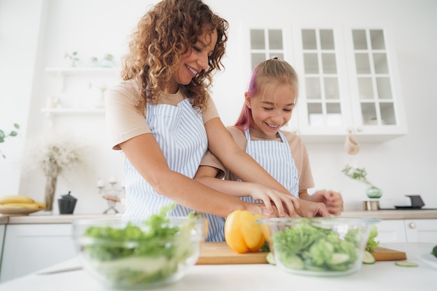 Mamma insegna a sua figlia adolescente a cucinare insalata di verdure in cucina