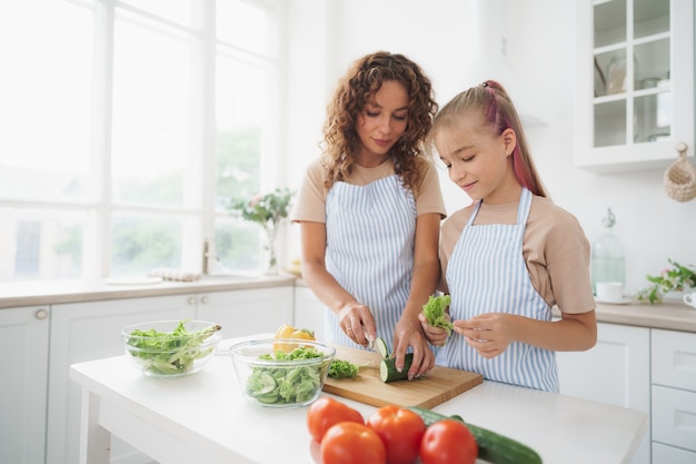 Mommy teaching her teen daughter to cook vegetable salad in kitchen