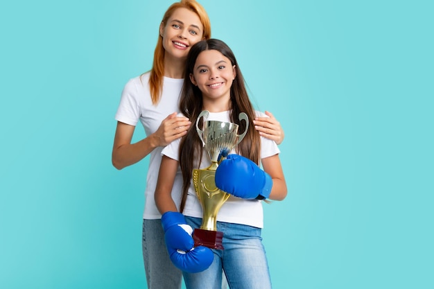 Mommy and teenager child daughter holding winning prize showing trophy against blue background Parent support girl child celebrating victory Little girl is practicing boxing girl teaches boxing