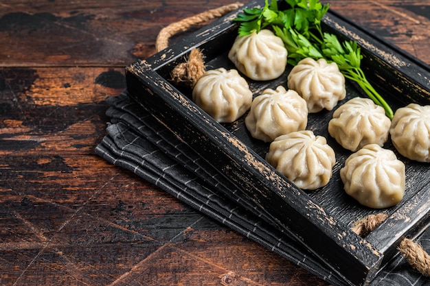 Momo dumplings in a wooden tray with herbs. Dark Wooden background. Top view. Copy space.