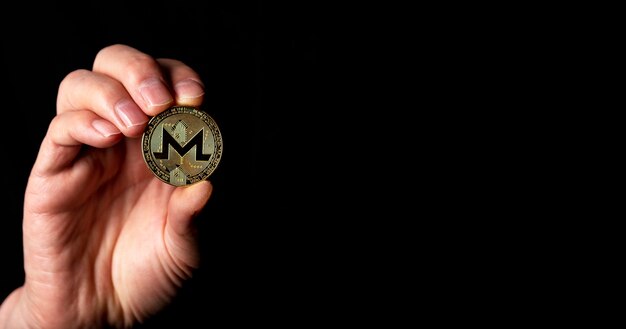 Золотая монета monero в мужской руке на черном фоне баннера с копией пространства для текста