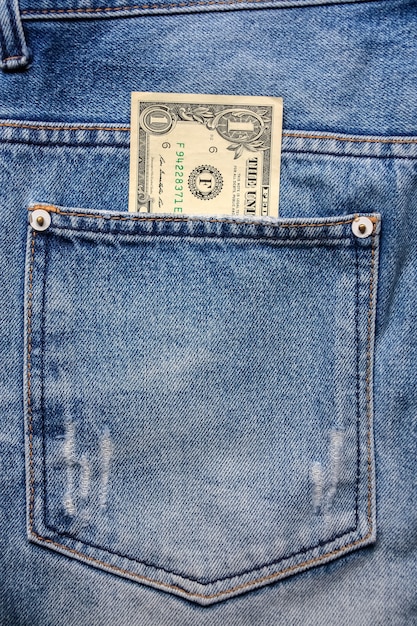 Деньги в заднем кармане джинсовой ткани синих джинсов.