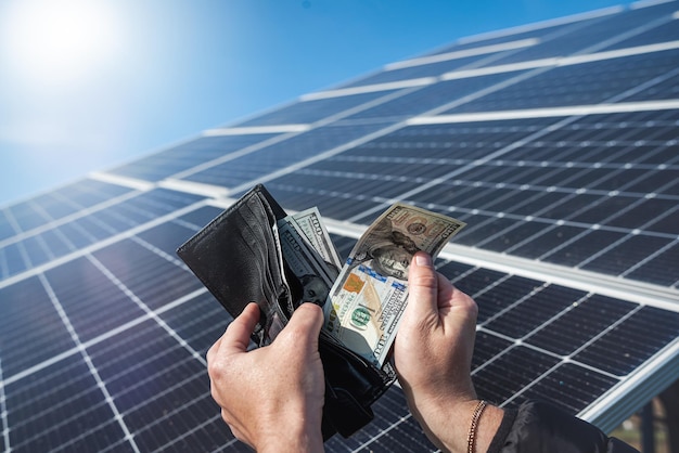 Money dollars in a wallet holding hands over a solar panel\
banknotes on the panel concept of cheap solar energy