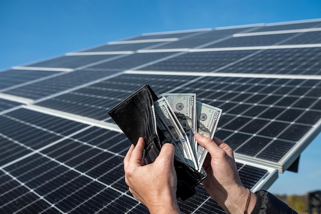 태양 전지 패널 위에 손을 잡고 있는 지갑에 있는 돈 패널에 있는 지폐 저렴한 태양 에너지의 개념