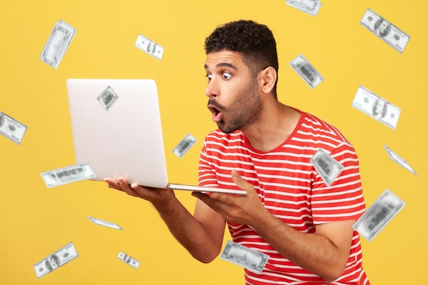 Money falling and shocked rich man looking at laptop screen