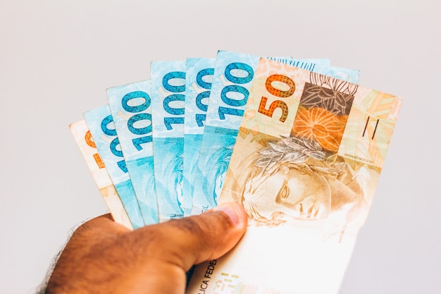 Photo money from brazil. real notes, brazilian money in the hand of a black man. notes of 100 and 50 reais. concept of inflation, economy and business. light background