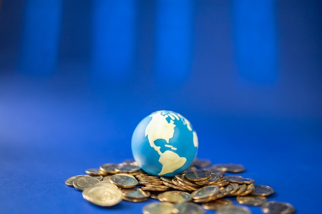 Money Global Business Concept. Closeup of mini world ball on pile and gold coins on blue background.