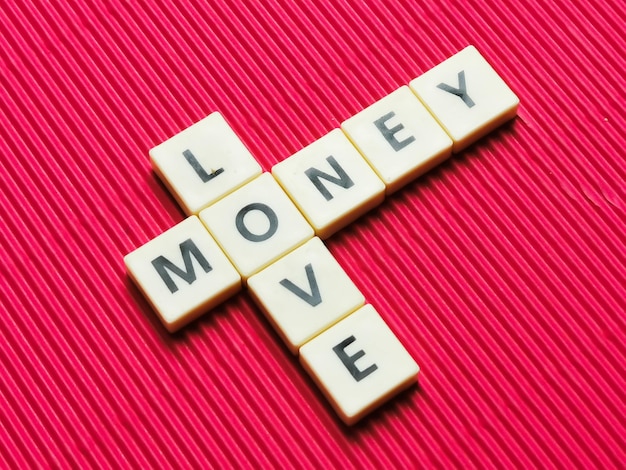 Money love crossword made from square letter tiles on red\
background.