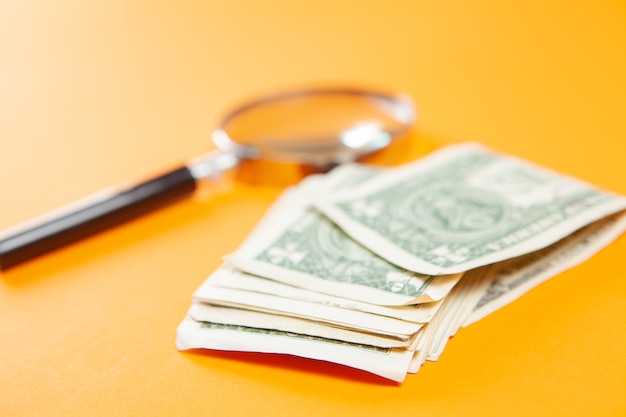 Money and magnifier on orange surface