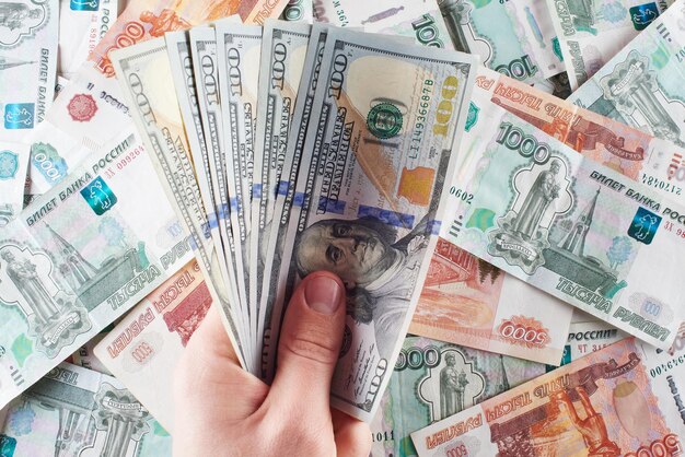 Money. Male hand holds American hundred dollar bills against the background of Russian paper rubles.