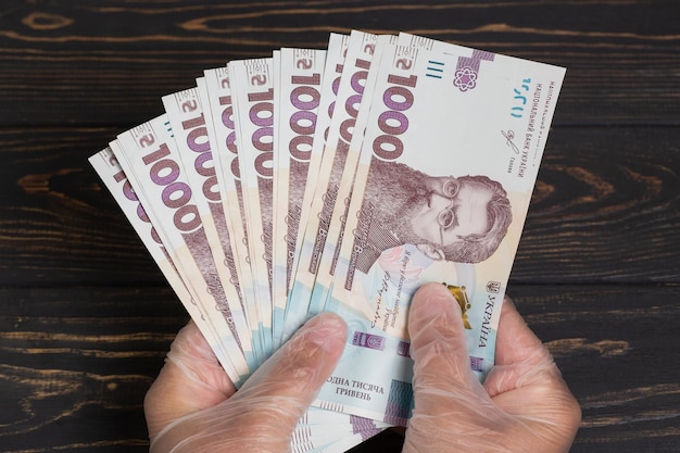 写真 ウクライナのお金。木製のテーブルに手袋をはめた手でウクライナグリブナ紙幣のスタック。グリブナ1000uah