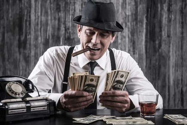 Money and power. senior gangster in shirt and suspenders counting money and smiling while sitting at the table