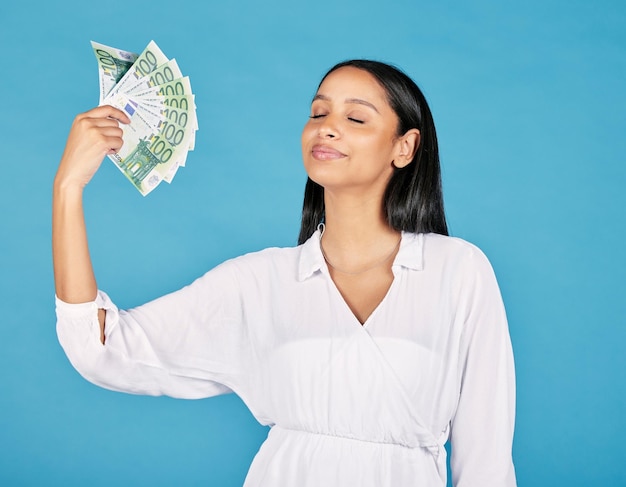 Money wealth and rich woman holding fan of cash and cooling herself ready to blow or spend it all Female lottery winner embracing luck success and win in the studio on a blue background