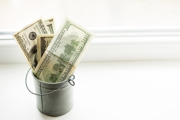 Moneybox, dollars in bucket on white window.light background. 