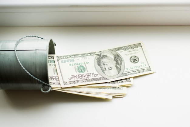 Photo moneybox, dollars in bucket on white window.