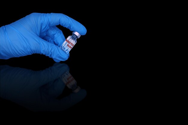 The monkeypox vaccine in a hand in a blue medical glove on a black mirror background