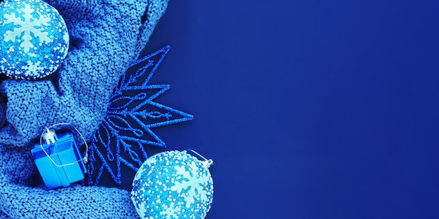 Monochrome blue banner: knitted fabric, Christmas toys and a shiny Christmas star on a blue background. Flat layout, top view, space for copy.
