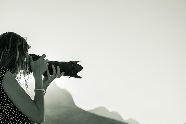 日の出の外でデジタル一眼レフカメラで写真を撮る若い女性のモノクロ画像