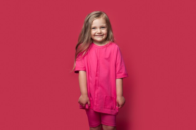 Photo monochrome photo of a caucasian small blonde girl smiling at camera in casual clothes on a red studio wall