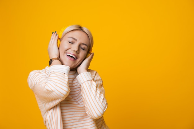 Monochrome photo of a caucasian woman listening to musing from headphones on a yellow wall with free space