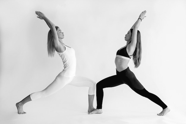 monochrome portrait of blonde and brunette beautiful cheerful fit women doing yoga asanas