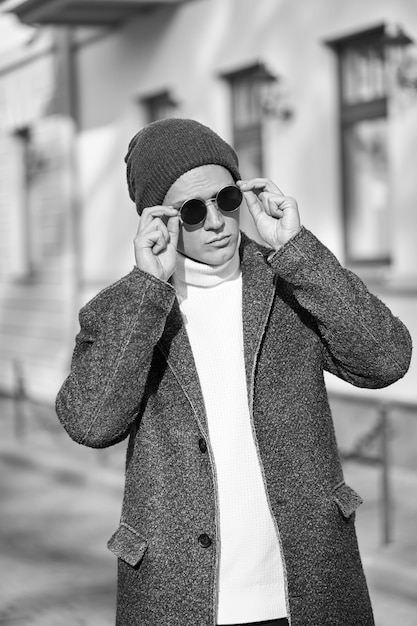 Monochrome portrait of fashionable stylish young attractive hipster man in sunglasses wearing a coat