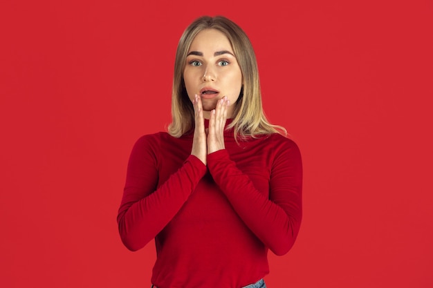 Monochrome portrait of young caucasian blonde woman isolated on red studio wall.