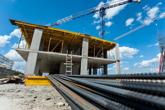 Monolithic frame with metal fittings of a new house under construction against the background of a crane and blue sky