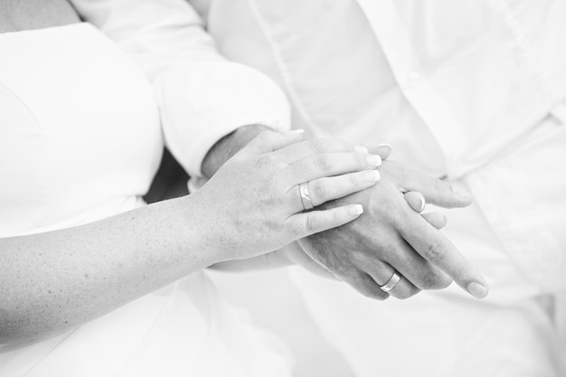 Monotone shot of couple holding hands wear rings with bits of sand, black and white