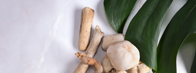 Photo monstera leaf with stones and wooden sea sticks on a marble background background for eco products cosmetics