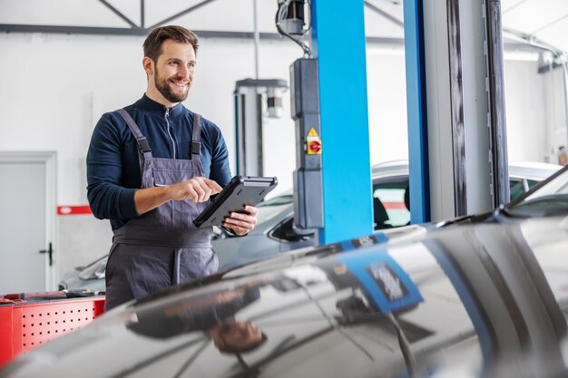 Monteur die tablet gebruikt voor het diagnosticeren van een autoprobleem. garage van auto salon interieur.