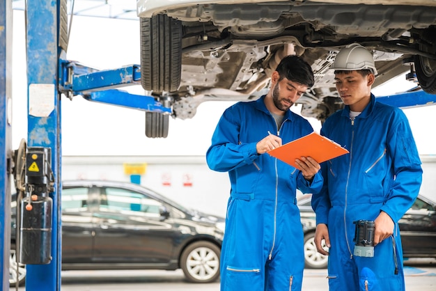 Monteur in blauw werkkleding-uniform inspecteert de bodem van de auto met zijn assistent automobile repareren