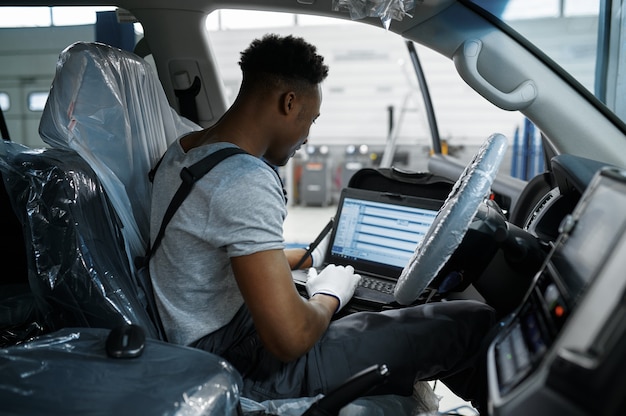 monteur man met laptop bij de auto met geopende kap in mechanische werkplaats