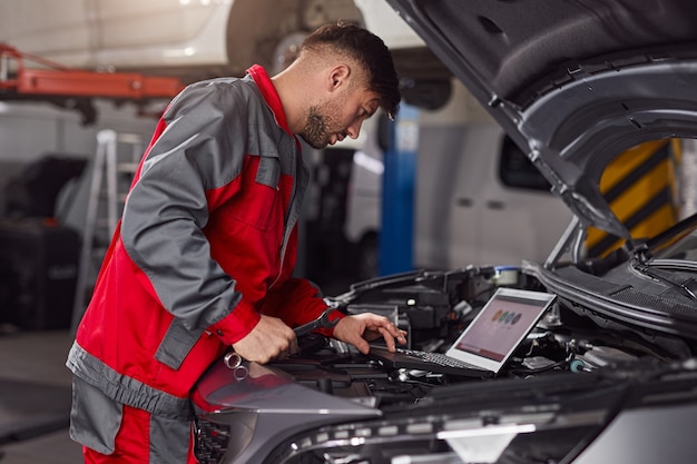 monteur met behulp van laptop tijdens het repareren van de motor van het voertuig