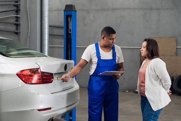 Foto monteur met klembord bespreekt autoreparatie met vrouw