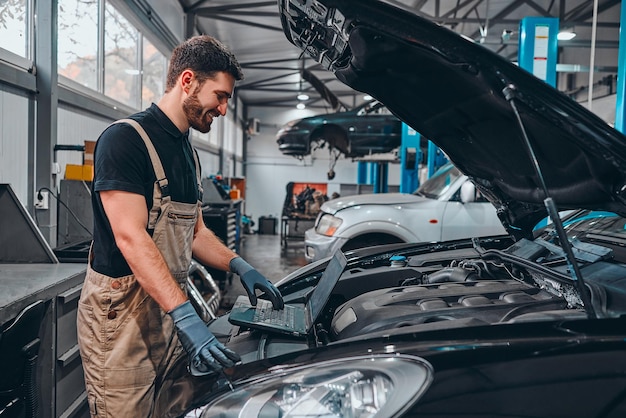 Monteur met laptop in de buurt van automotor Modern auto diagnostisch programma Autoserviceconcept Zijaanzicht