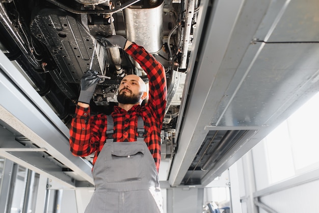 Monteur werkt onder auto bij de reparatie-garage. Automonteur die in garage werkt. Reparatie service.