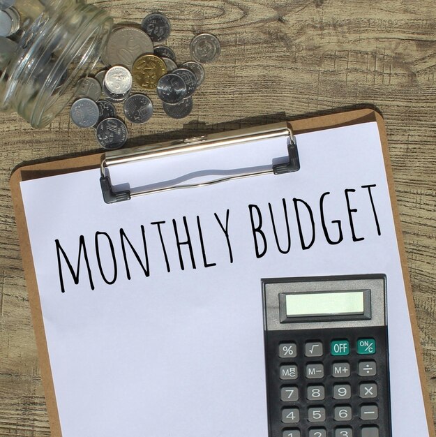 Budget mensile testo scritto sulla calcolatrice appunti di carta e vaso di vetro pieno di monete