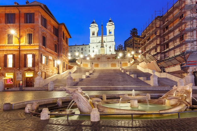 Scalinata monumentale piazza di spagna, vista da piazza di spagna, e la fontana del primo barocco chiamata fontana della barcaccia o fontana della brutta barca durante l'ora blu mattutina, roma, italia.