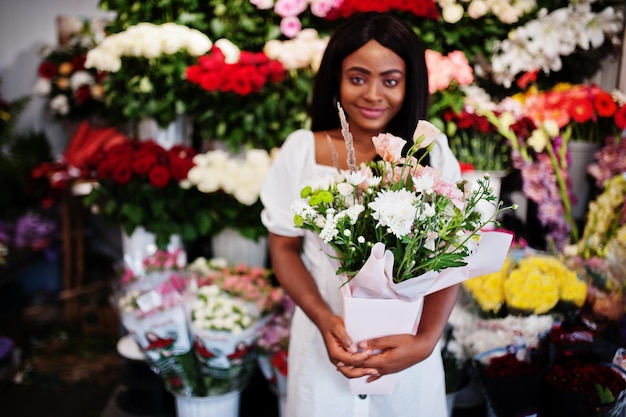 Mooi Afrikaans Amerikaans meisje in tedere witte jurk met boeket bloemen in handen permanent tegen florale achtergrond in bloemenwinkel Zwarte vrouwelijke bloemist