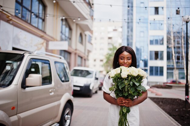 Mooi Afrikaans Amerikaans meisje met boeket van witte rozen bloemen op dating in de stad. Zwarte zakenvrouw met bos bloemen in de buurt van auto.