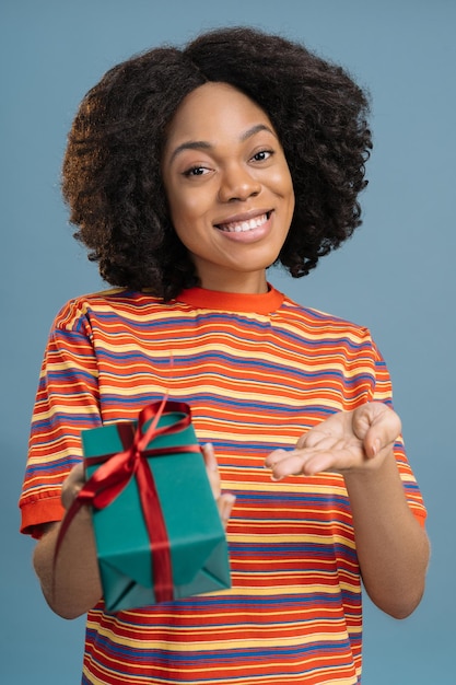 Mooi Afrikaans Amerikaans meisje met geschenkdoos kijken naar camera geïsoleerd op blauwe achtergrond